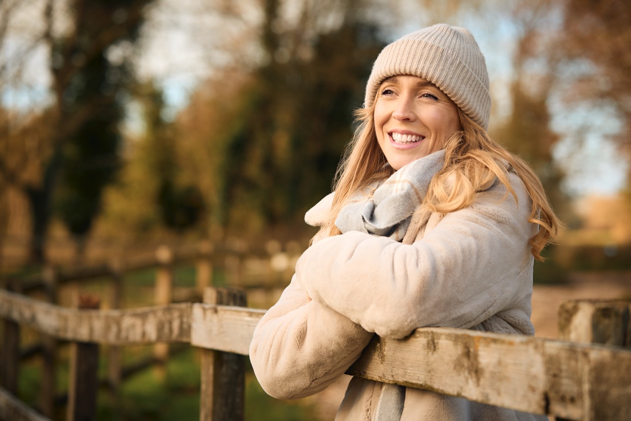 Woman leaning on wooden fence in autumn clothing